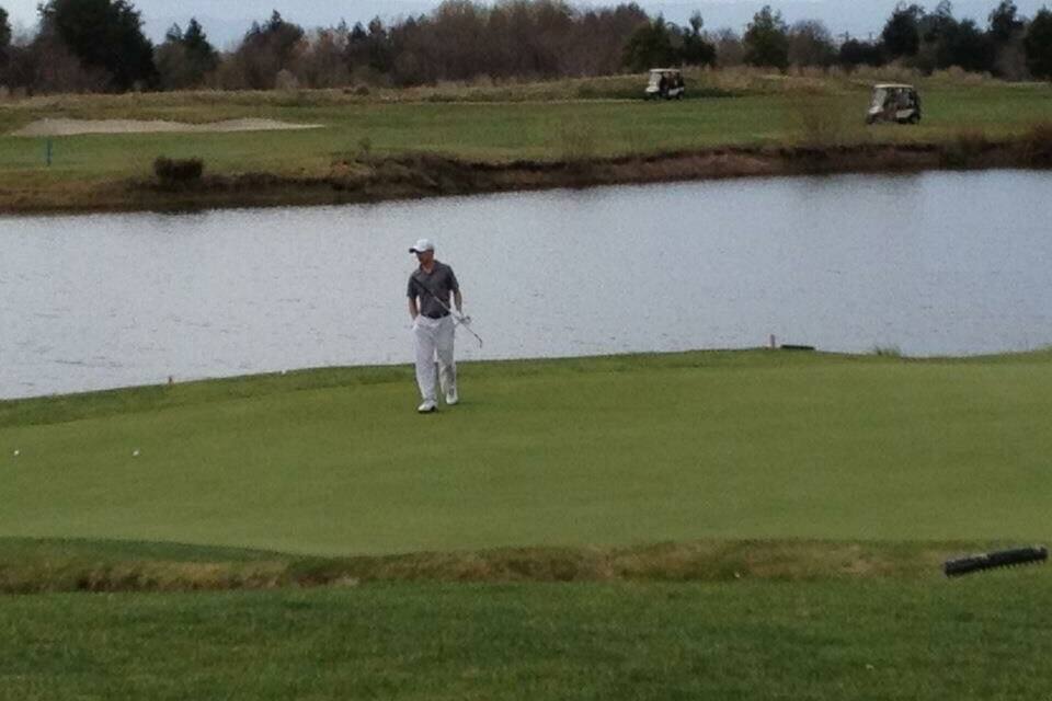 A golf course with a pond, a golf cart, and a hilly landscape in the background.
