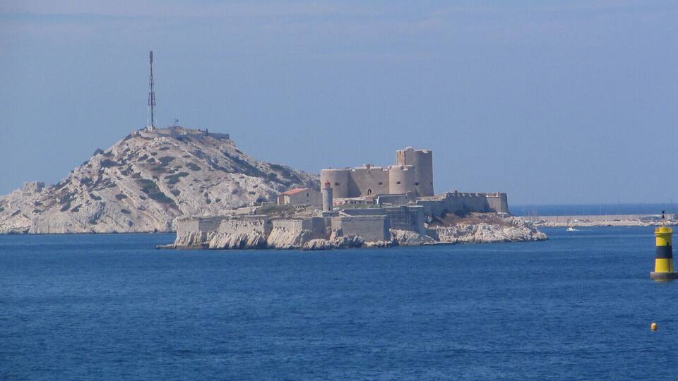 A coastal fortress on a rocky island with a lighthouse in the foreground.