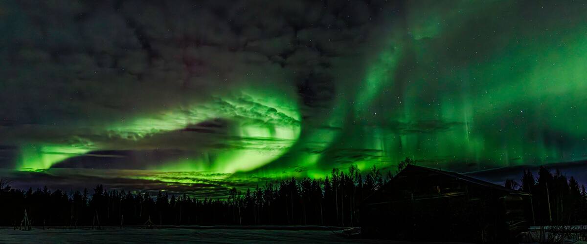 The Northern Lights over a snowy landscape with a cabin.