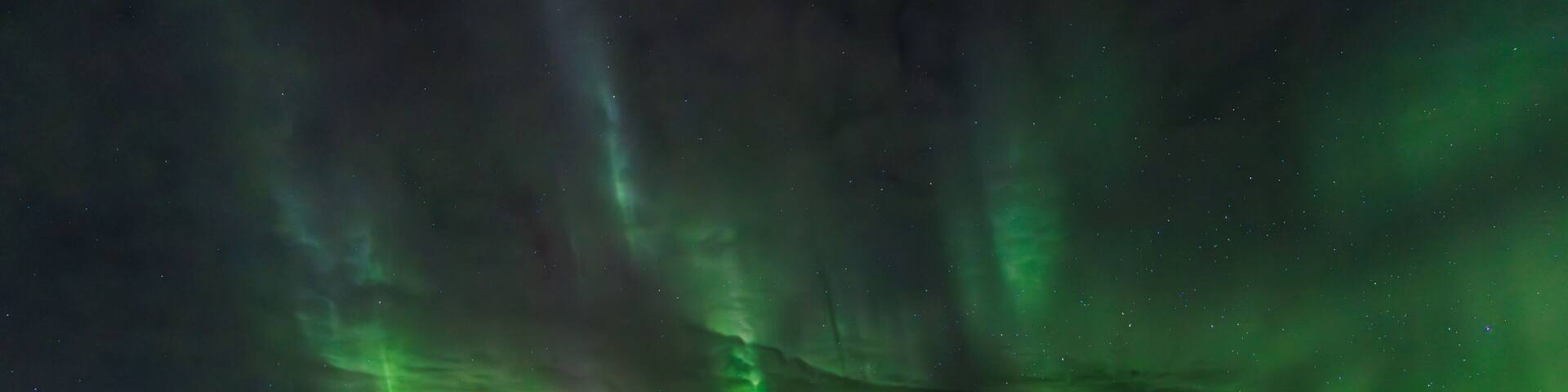 The Northern Lights over a snowy landscape with a cabin.