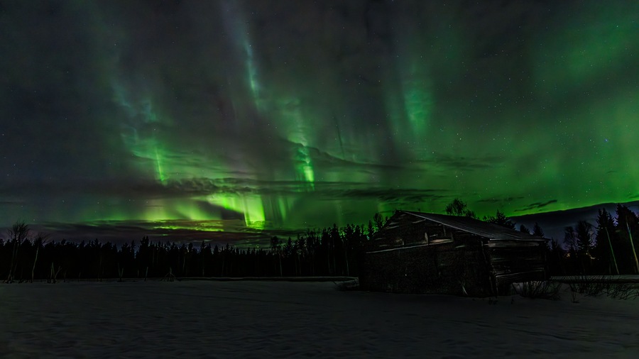 The Northern Lights over a snowy landscape with a cabin.