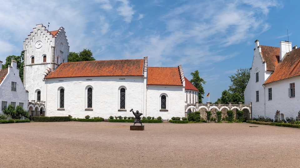 A historic white building with a red-tiled roof, a clock tower, and a statue in the courtyard.