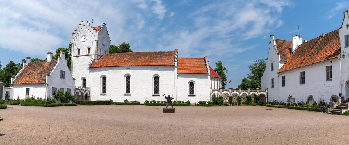 A historic white building with a red-tiled roof, a clock tower, and a statue in the courtyard.