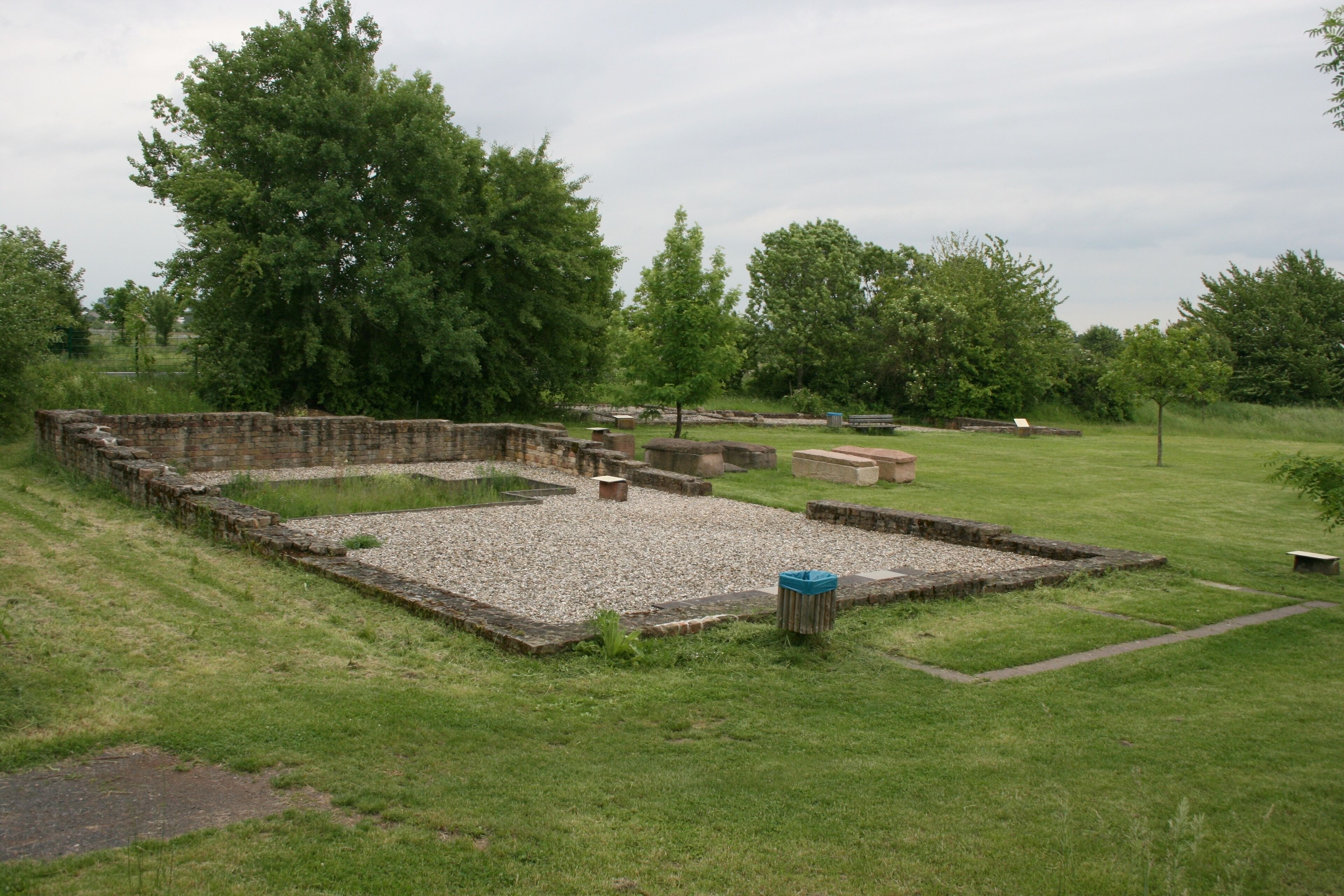 Römische Villa Wachenheim, Ansicht zweier Nebengebäude von Nordwesten. Im Vordergrund Speichergebäude D (mit Darre links und Räucherofen einer früheren Bauphase), im Hintergrund Stallgebäude B mit Wohntrakt C und Kanalheizung. Dazwischen spätantike Steinsarkophage.