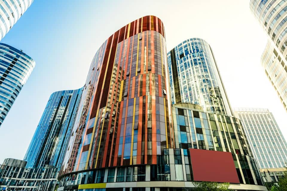 Un horizonte urbano moderno con edificios altos, fachadas de vidrio reflectante y una combinación de diseños arquitectónicos curvos y rectos.