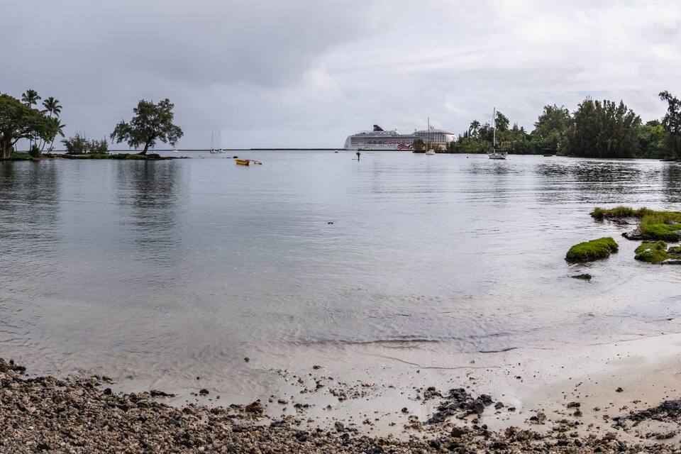 A calm lake with a cruise ship in the distance, surrounded by lush greenery and rocky shores.