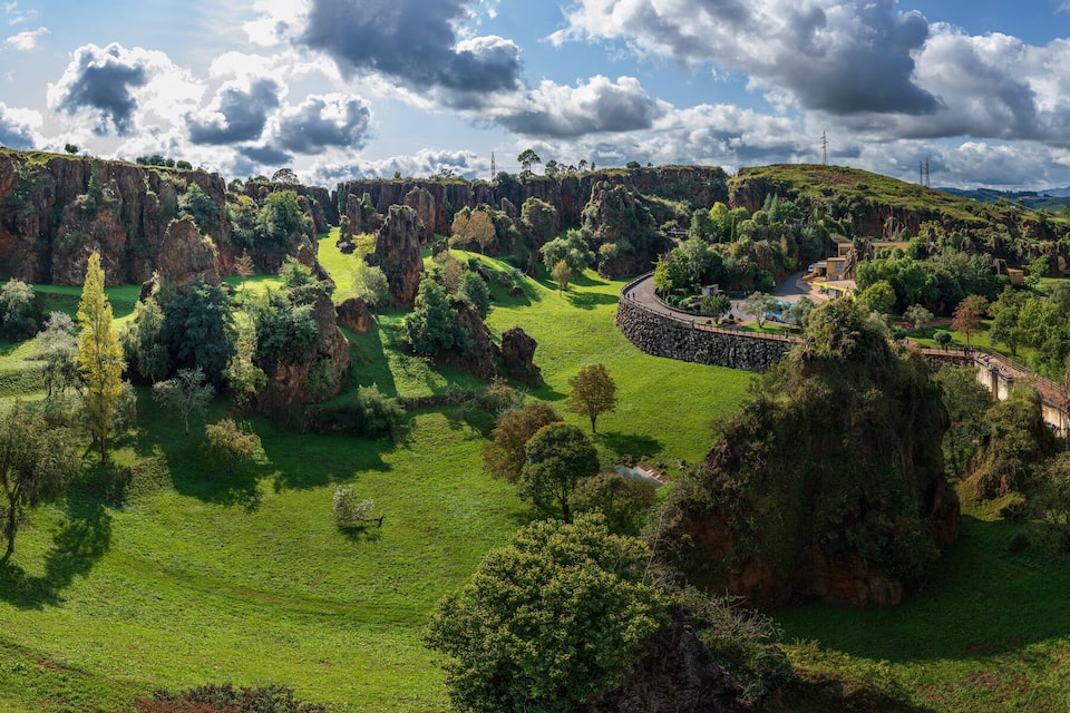 A lush valley with green fields, rocky cliffs, and scattered trees.