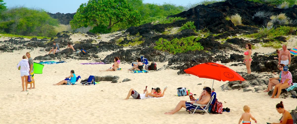 A sandy beach with people relaxing, a red umbrella, and rocky outcrops.