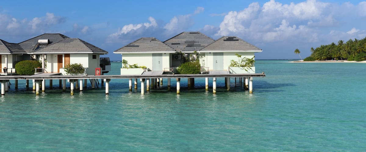 Overwater bungalows on stilts, clear turquoise water, and a sandy beach with palm trees.