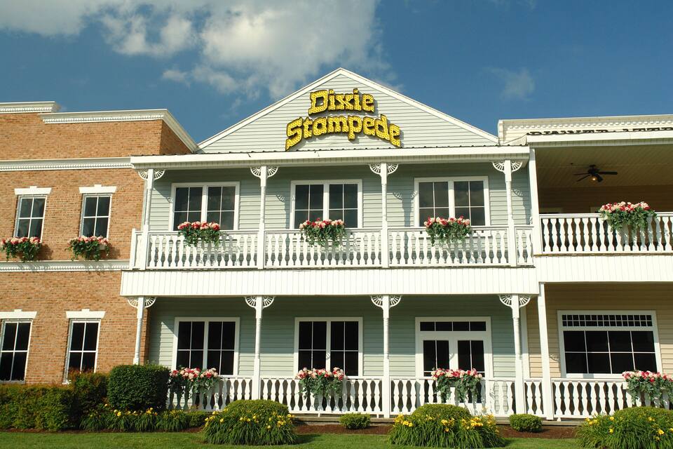 A two-story building with a sign reading "Dixie Stampede." It has a white facade, multiple windows, and a balcony with flower boxes.