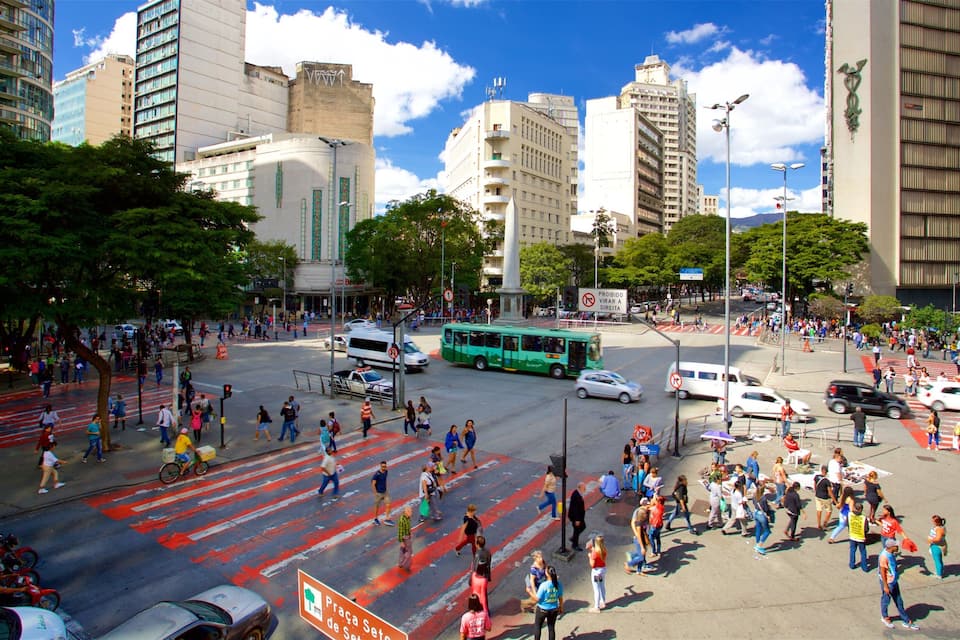Um movimentado cruzamento urbano com pedestres, veículos e um ônibus verde.