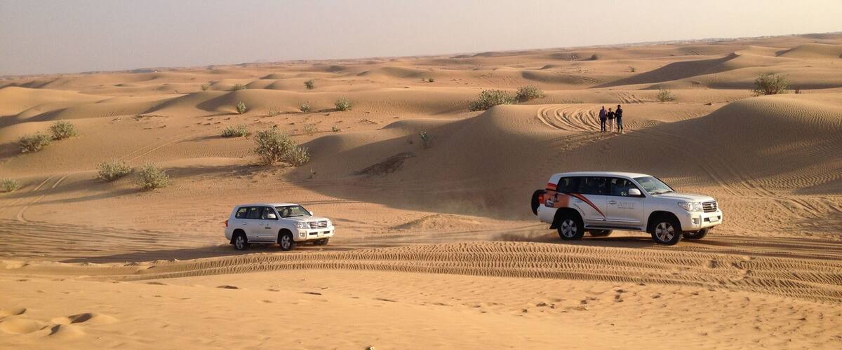 A desert landscape with sand dunes and two vehicles.