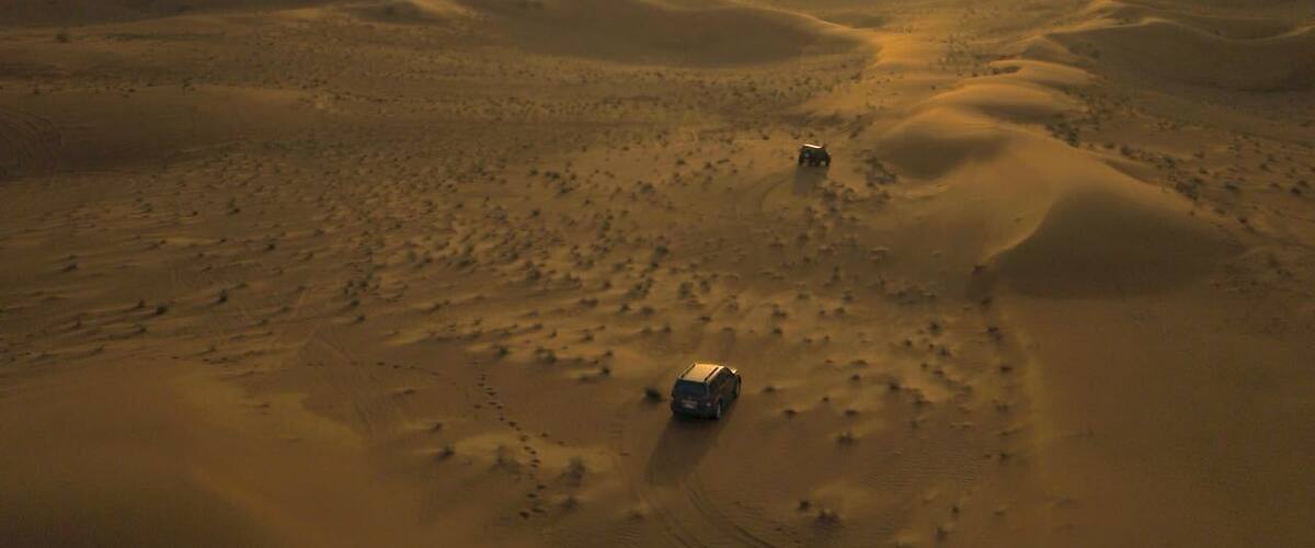 A desert landscape with sand dunes and two vehicles.