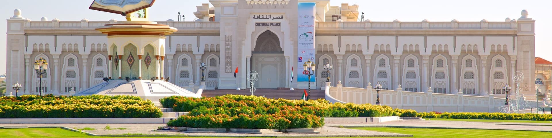 A large white building with a dome and a central entrance. There are flags and a sign in front.