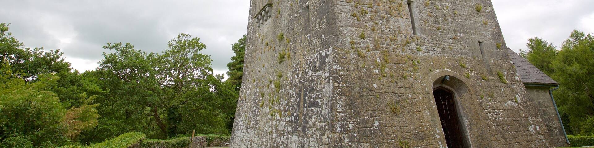 A tall stone tower with moss growth, surrounded by lush greenery and trees.