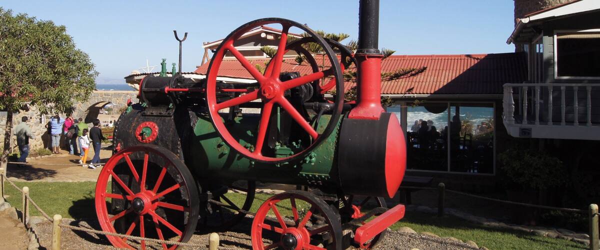 A vintage tractor with red wheels and a black body, parked in a grassy area with a building in the background.