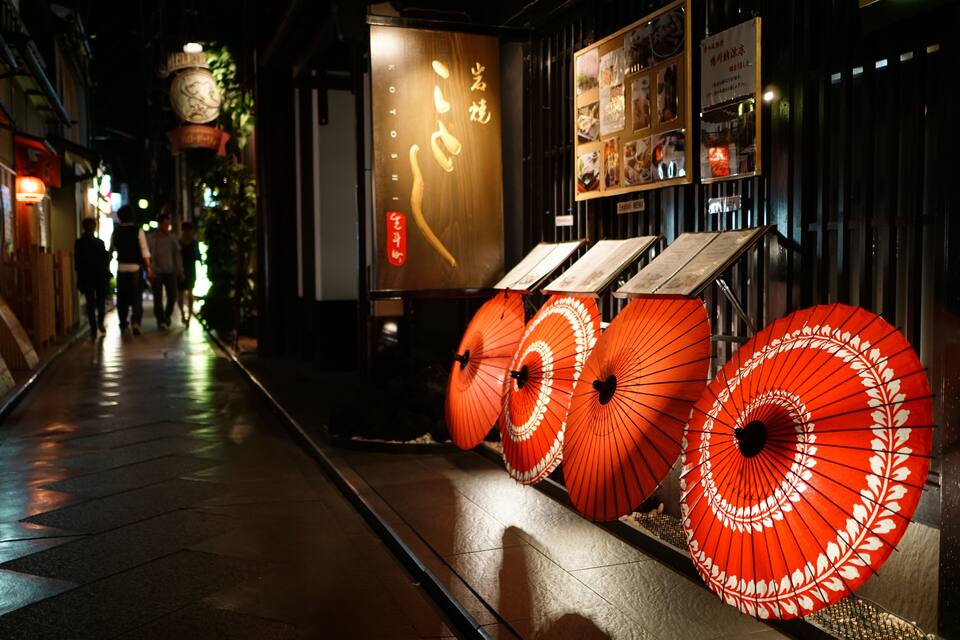 Une rue bordée de parasols rouges et un restaurant dont l’enseigne est en japonais.