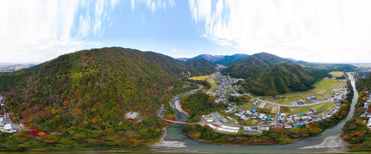 A river winding through a valley with mountains in the background and a small town with buildings and roads along the riverbanks.