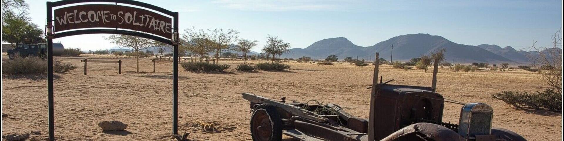 An old truck in a desert with a 'Welcome to Solitude' sign.