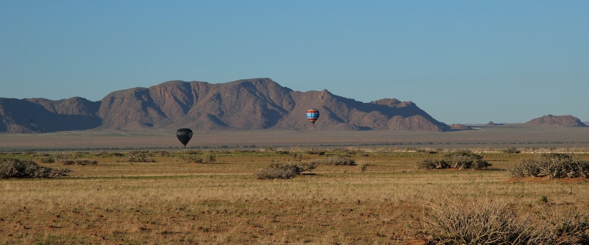 A hot air balloon in a desert landscape with mountains in the background.