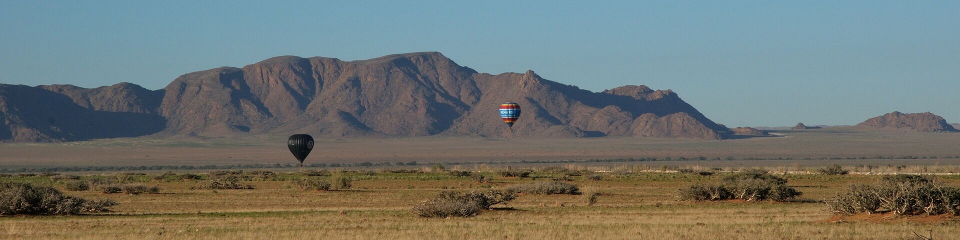 A hot air balloon in a desert landscape with mountains in the background.