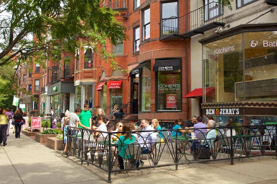 A sidewalk lined with brick buildings, outdoor cafes, and pedestrians.