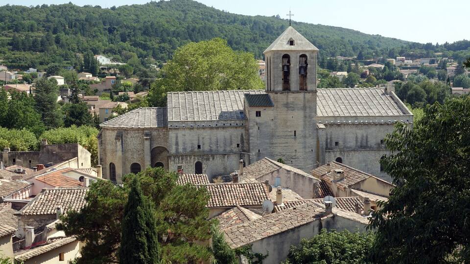 A historic church with a bell tower, surrounded by a town with terracotta roofs and lush greenery.