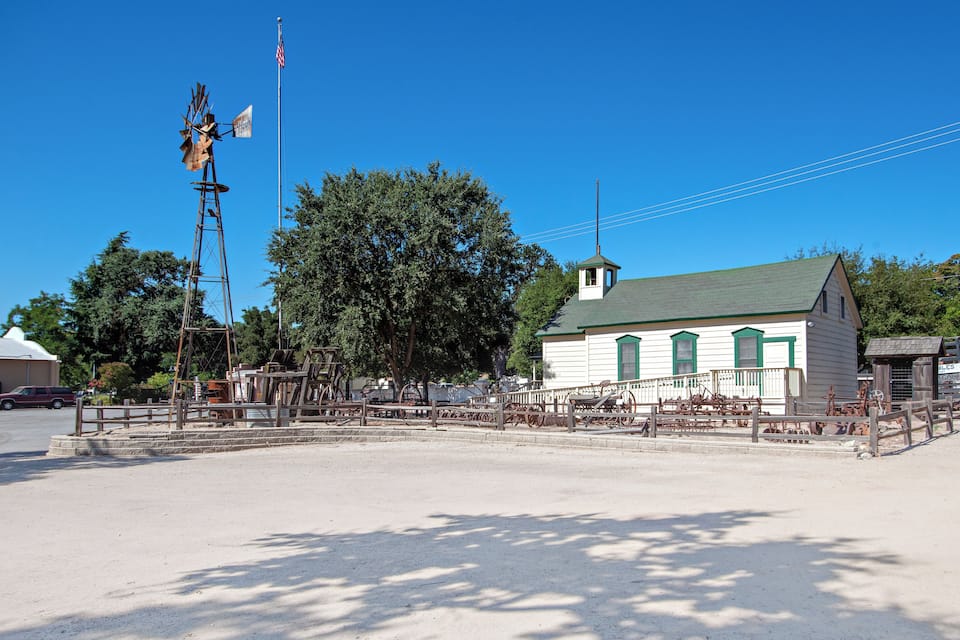 A historical building with a green roof, surrounded by a fence and various antique machinery.