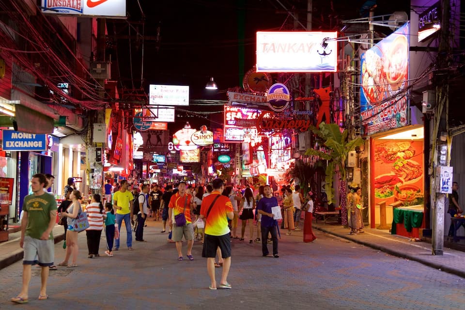 A bustling street at night with neon signs and crowded sidewalks.