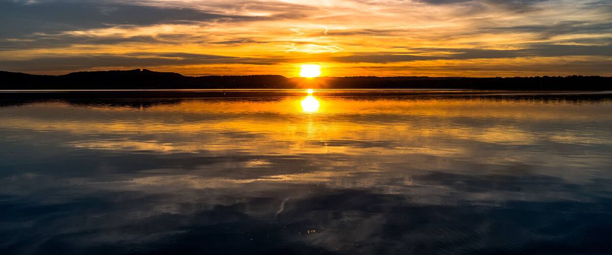 A sunset over a calm lake with reflections of the sun and clouds.