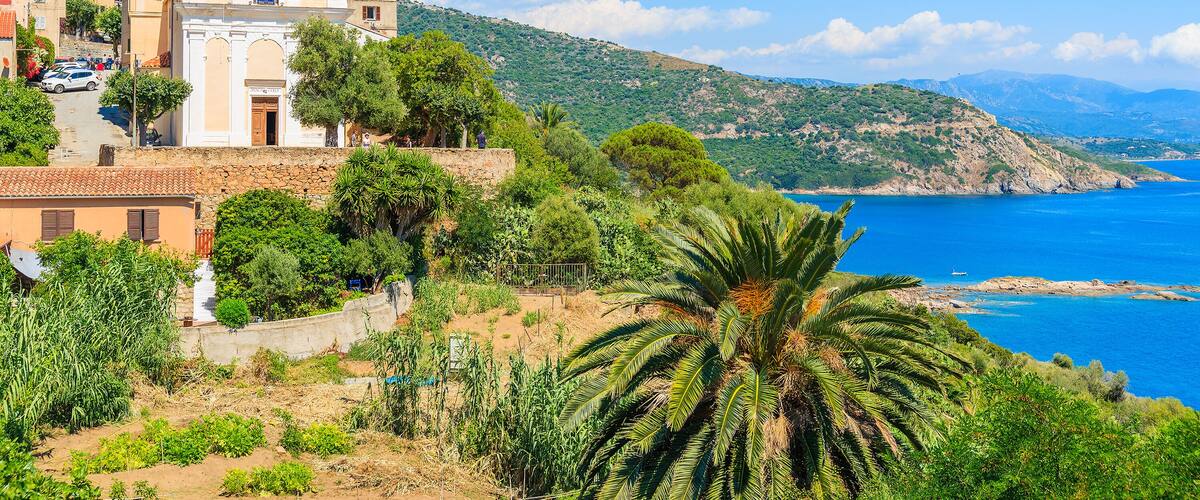 A coastal town with a church, palm trees, and a clear blue sea.