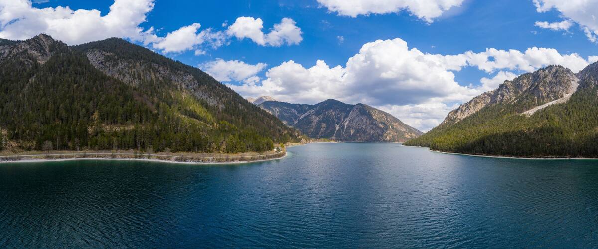 A calm lake surrounded by forested mountains under a partly cloudy sky.