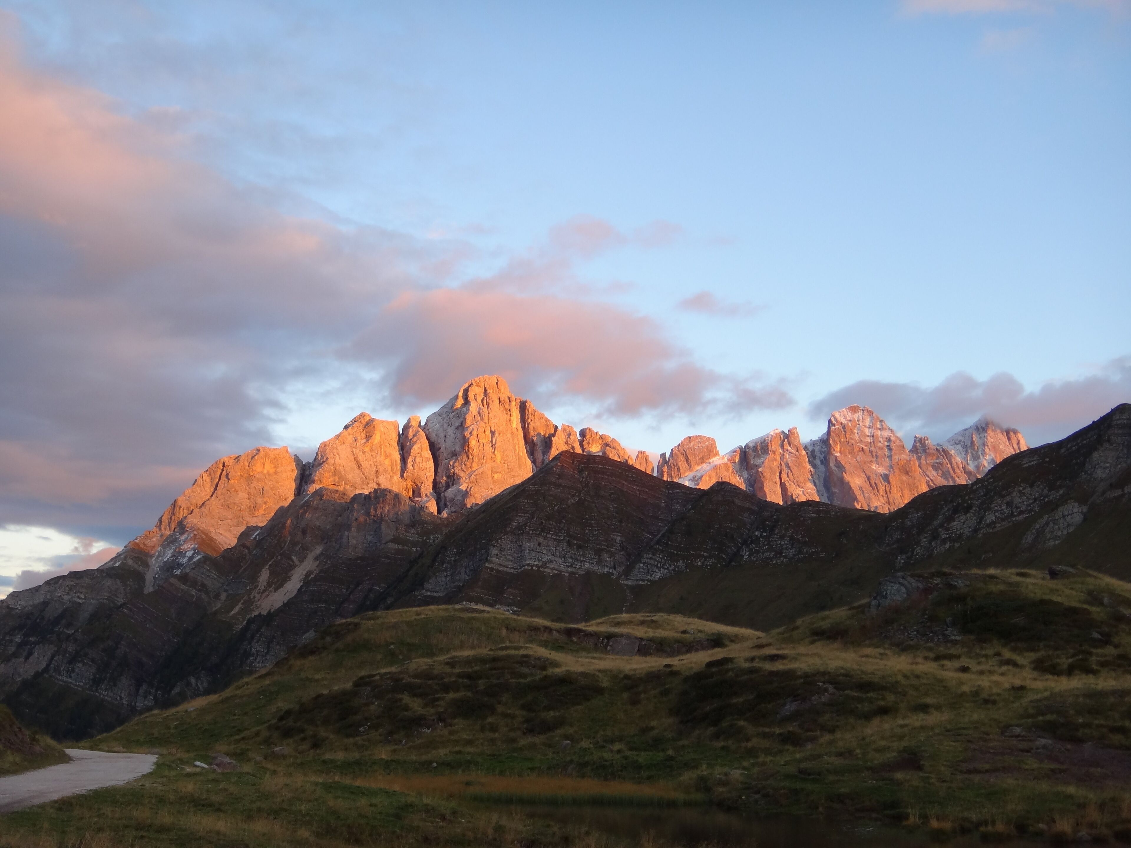 A mountain range with rugged peaks and a winding road leading through a grassy valley.