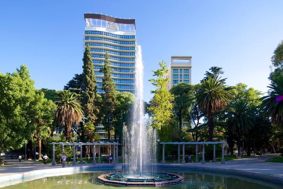 A fountain in a park with tall buildings in the background.