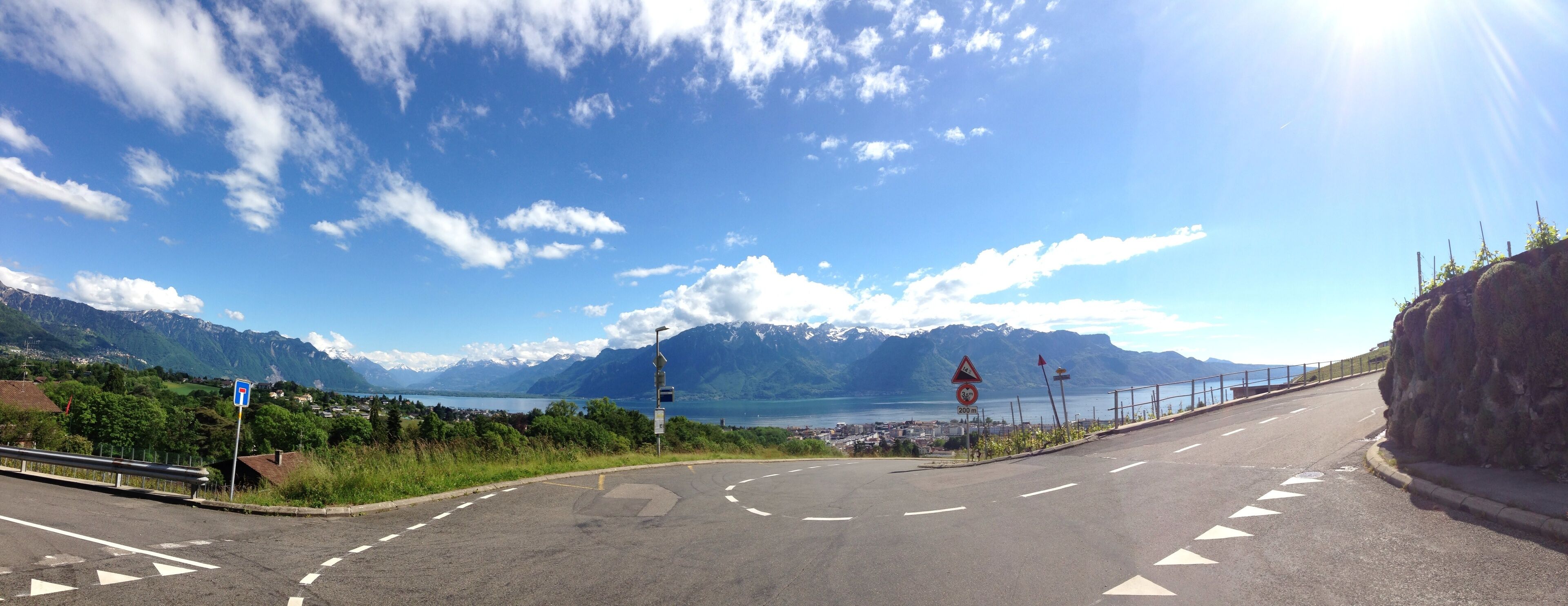 A road curving around a mountainous landscape with a lake and a town in the distance.