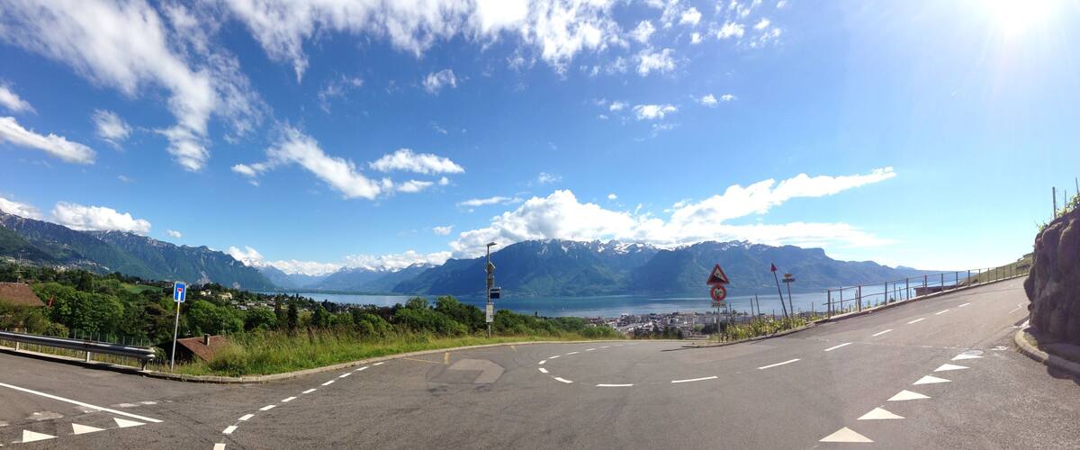 A road curving around a mountainous landscape with a lake and a town in the distance.