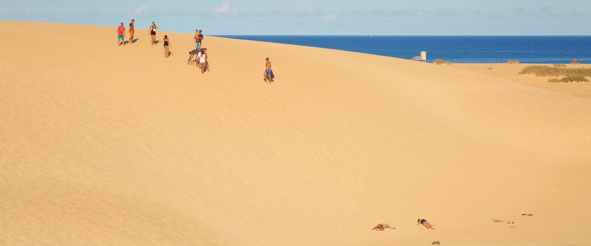A sandy beach with people walking and lying on the sand.