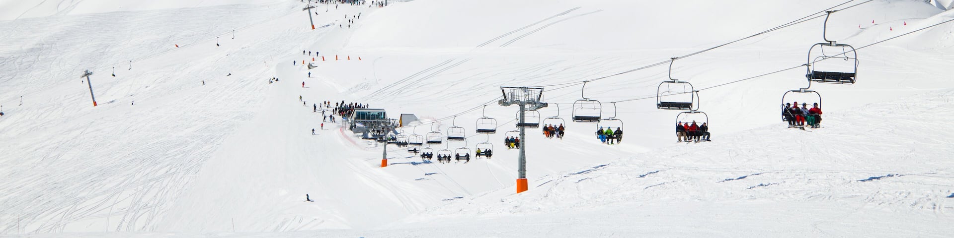 There are snow slopes of mountains from the pass of Tourmalet in the winter Pyrenees. Persons are being transported with a ski lift.