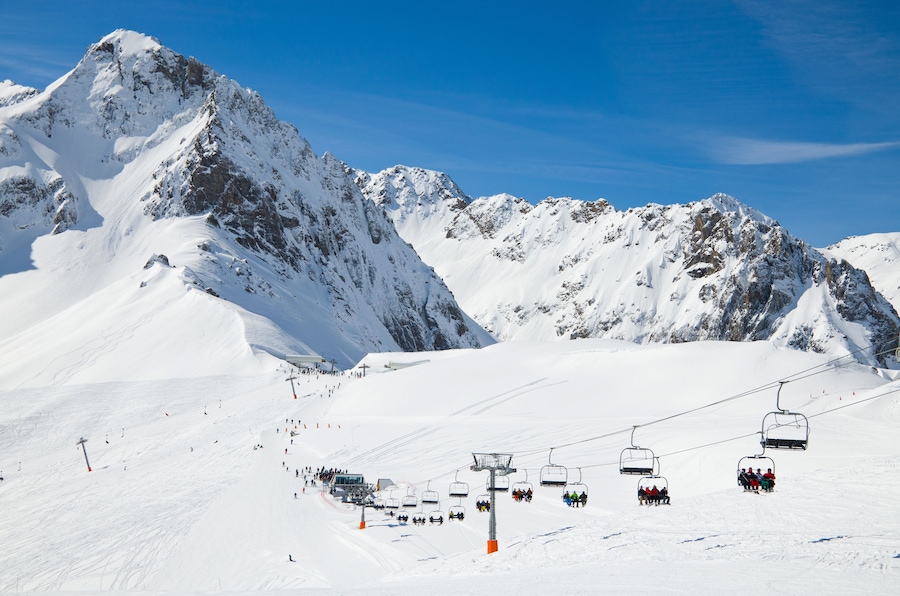 There are snow slopes of mountains from the pass of Tourmalet in the winter Pyrenees. Persons are being transported with a ski lift.