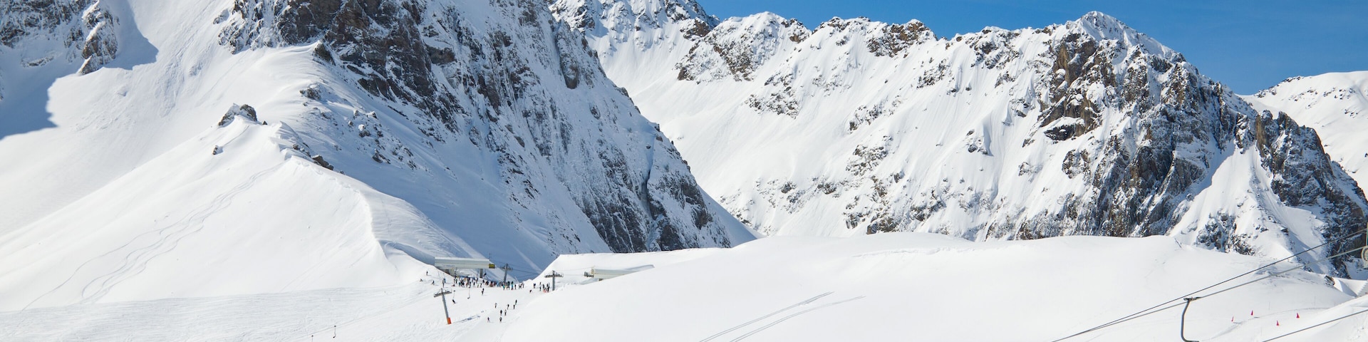 There are snow slopes of mountains from the pass of Tourmalet in the winter Pyrenees. Persons are being transported with a ski lift.