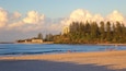 A beach with people walking, a building, and a forested hill.