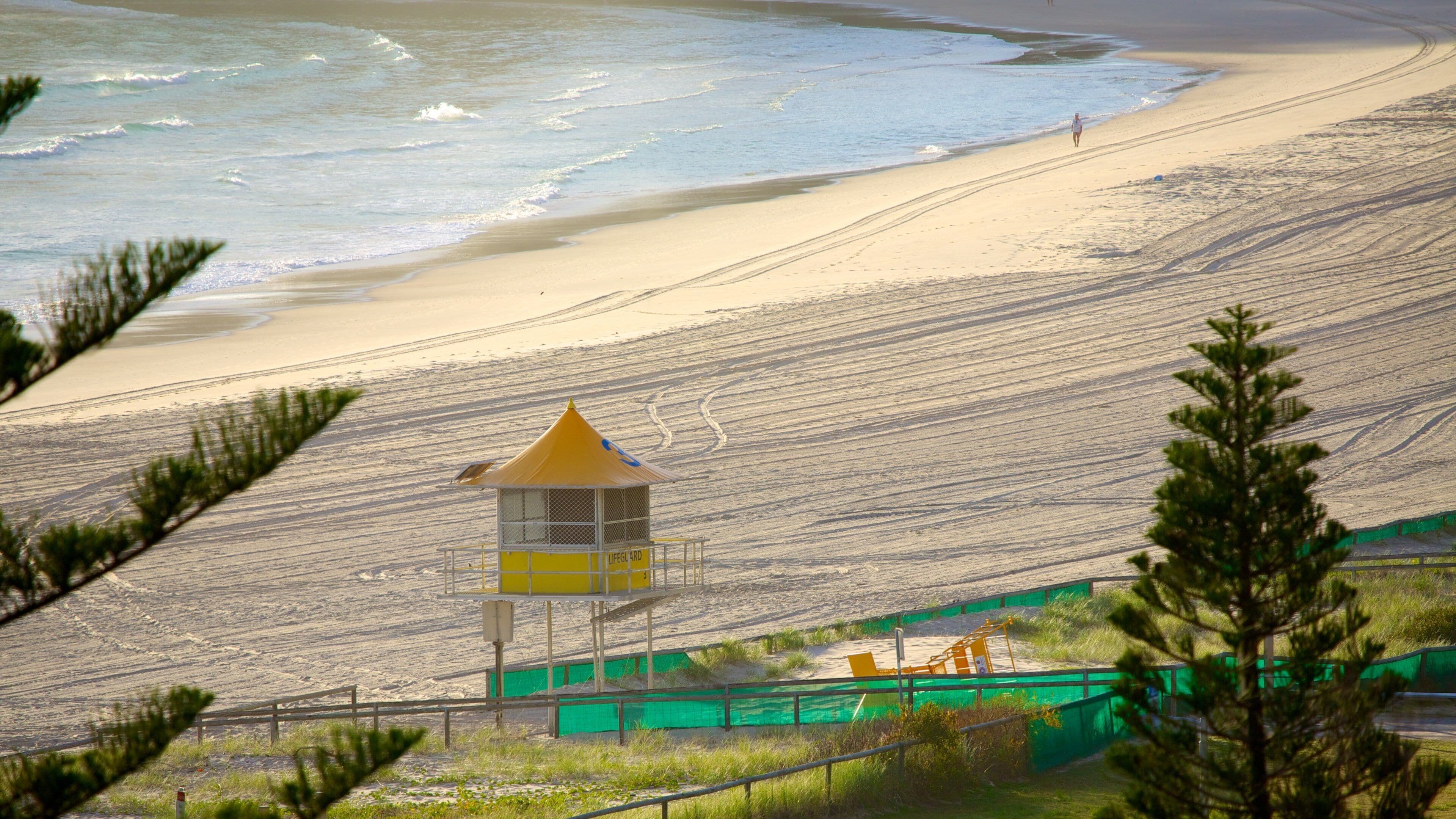 Une plage avec une tour de surveillance, des vagues et une personne qui se promène sur le sable.