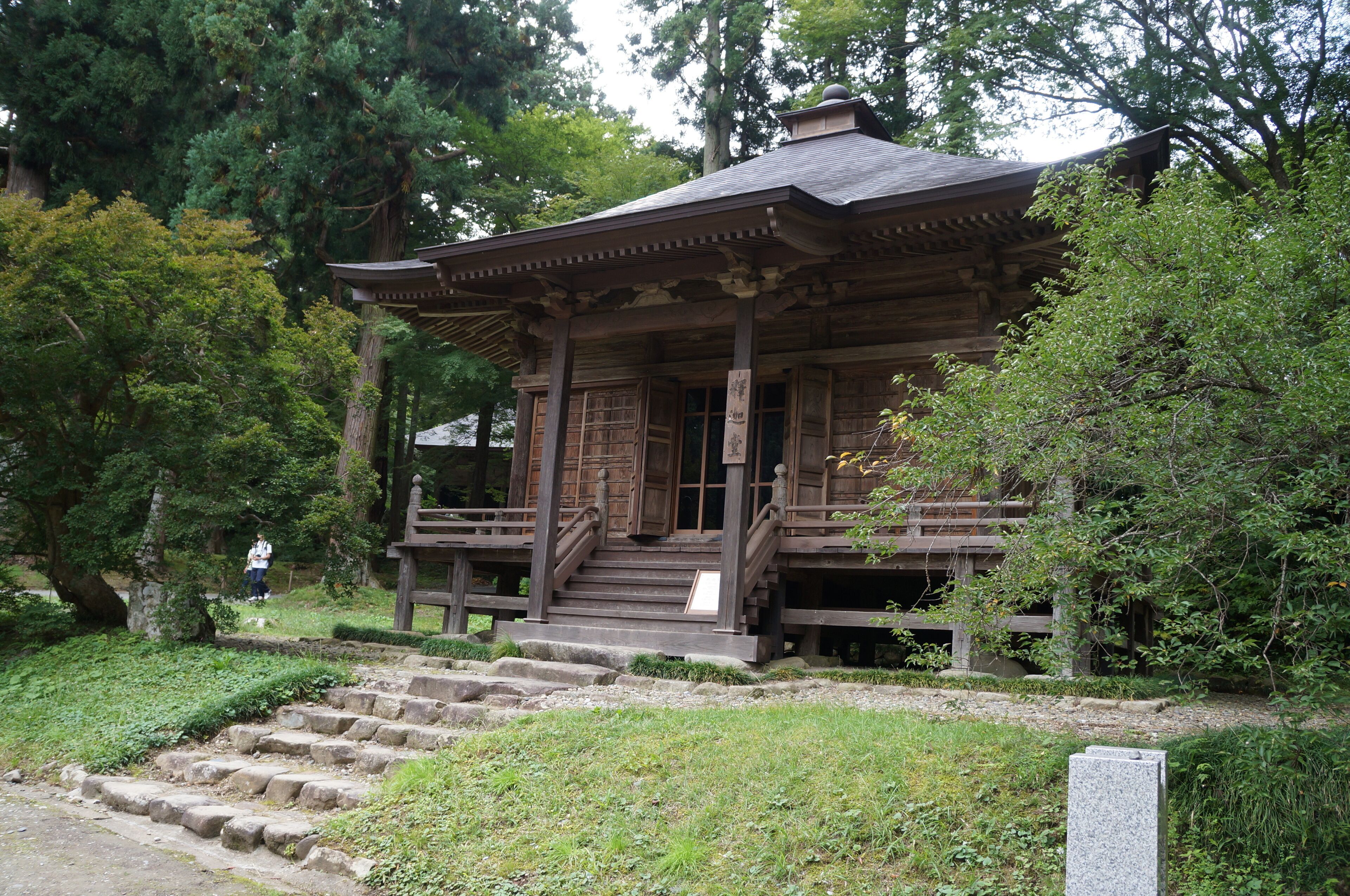 A traditional wooden structure with a tiled roof, surrounded by lush greenery and trees.