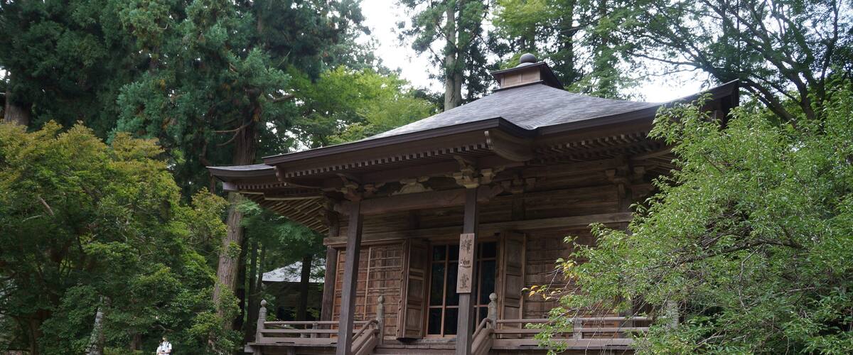 A traditional wooden structure with a tiled roof, surrounded by lush greenery and trees.