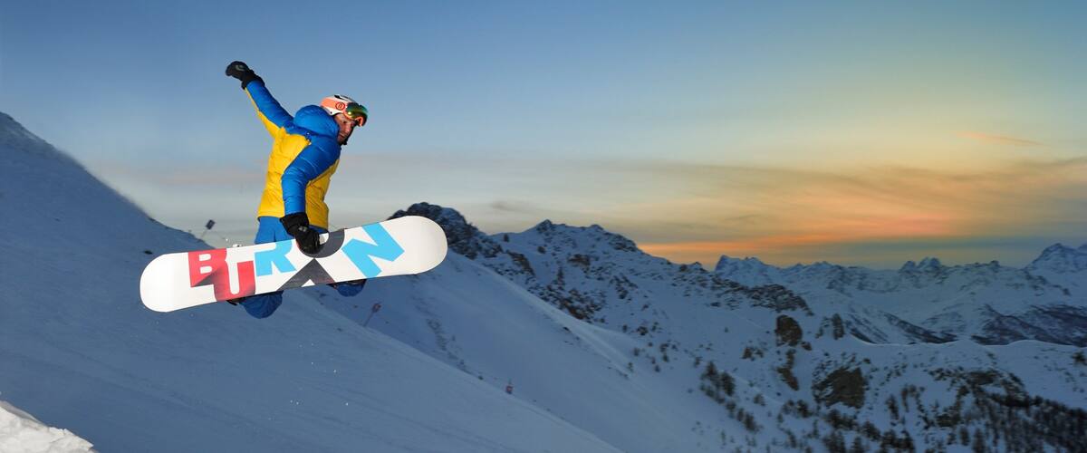 A snowboarder mid-air against a mountainous backdrop during sunset.