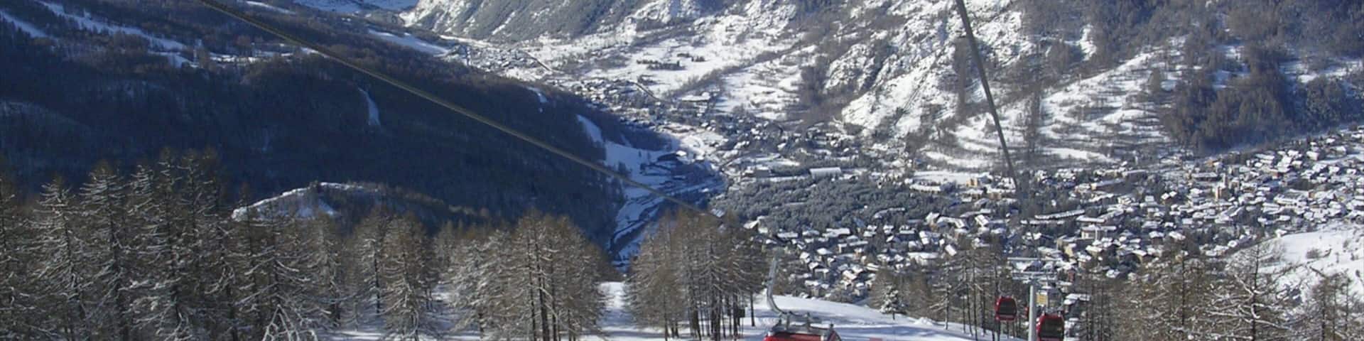 A ski lift in a snowy mountain area with a town below and snow-covered peaks in the background.