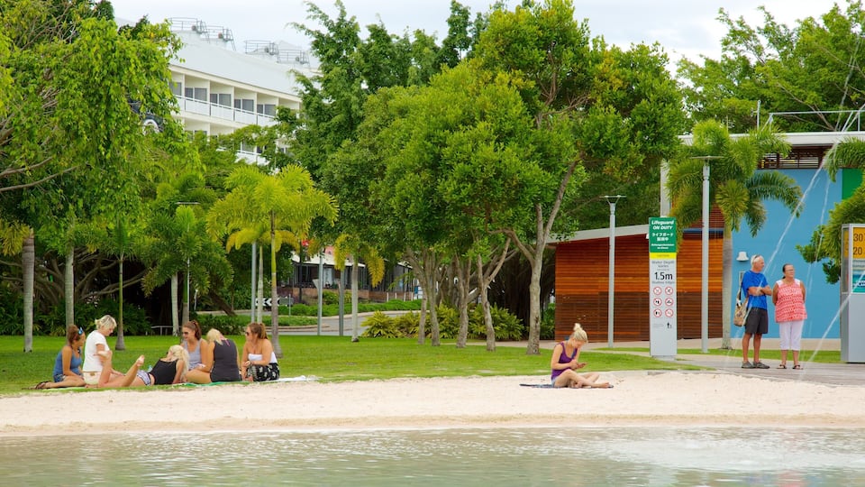 Una playa con gente relajándose, un letrero de socorrista y abundante vegetación.