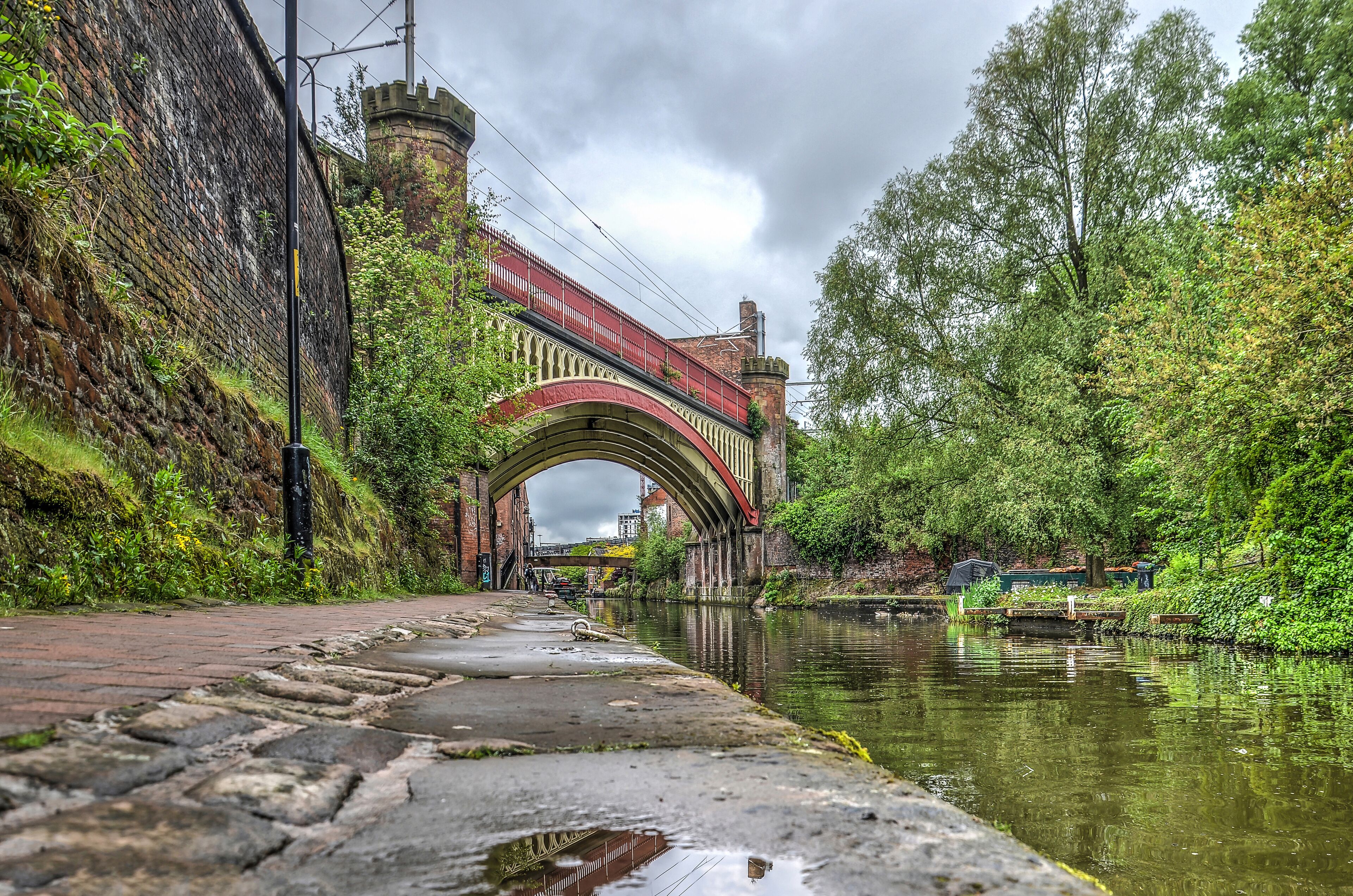 View from the footpath along Rochdale canal in the Castlefield area in the center of Manchester, England towards a historic steel railway bridge
