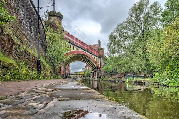 View from the footpath along Rochdale canal in the Castlefield area in the center of Manchester, England towards a historic steel railway bridge