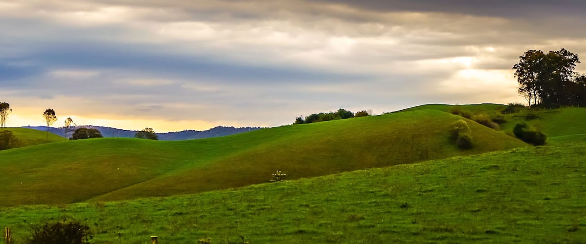 Rolling green hills with a mountain range in the background and a cloudy sky.